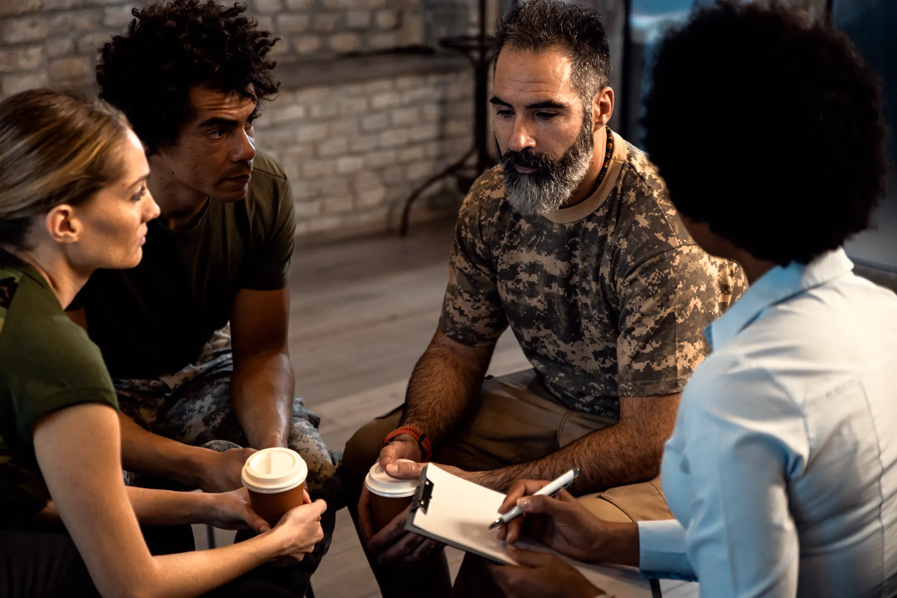 Veterans sitting in a group therapy session with a clinician taking notes